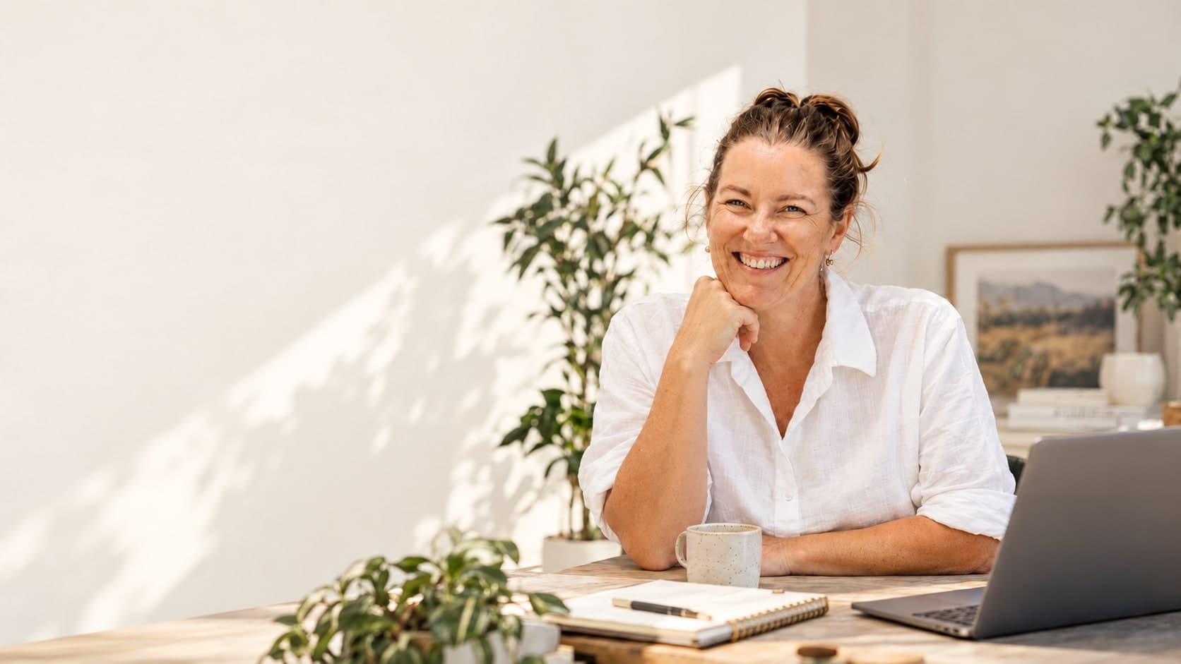 Kathryn Weekley smiling at her desk with a laptop, notebook and coffee cup